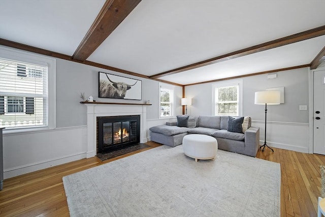 living area featuring a fireplace with flush hearth, beamed ceiling, baseboards, and wood-type flooring