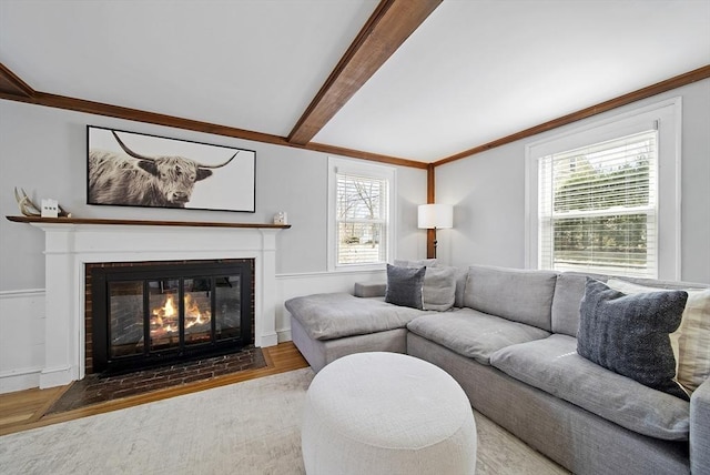 living area featuring beamed ceiling, a fireplace with flush hearth, wood finished floors, and ornamental molding