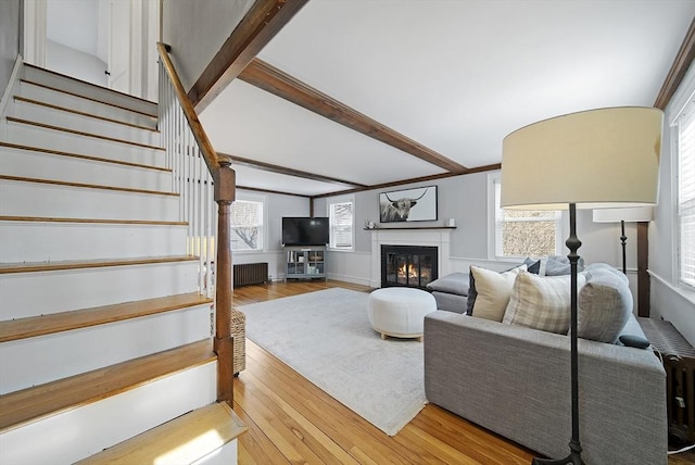 living room with stairway, light wood-style flooring, radiator heating unit, plenty of natural light, and a glass covered fireplace