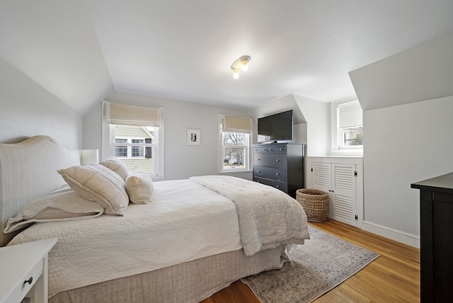 bedroom featuring baseboards, light wood-type flooring, multiple windows, and lofted ceiling