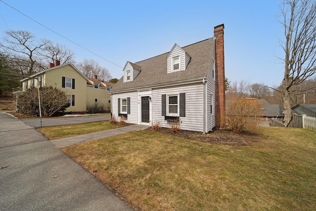 cape cod-style house with fence, a front yard, a chimney, and a shingled roof