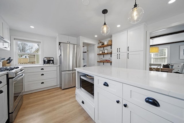 kitchen with decorative light fixtures, light stone counters, appliances with stainless steel finishes, light wood-style floors, and white cabinets