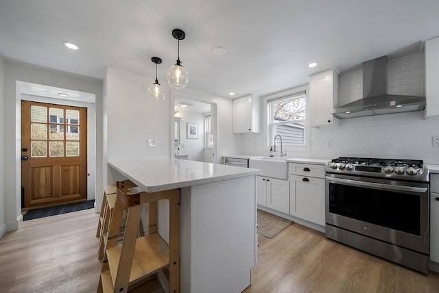 kitchen featuring wall chimney range hood, light wood-style flooring, stainless steel range with gas cooktop, and a sink