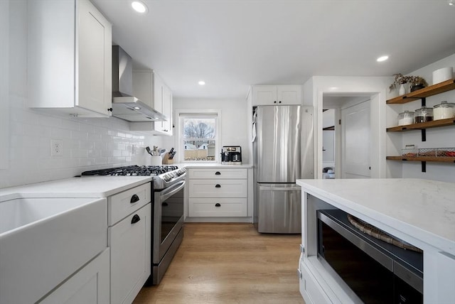 kitchen with light wood finished floors, appliances with stainless steel finishes, light countertops, and wall chimney range hood