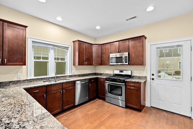 kitchen featuring light wood finished floors, visible vents, light stone counters, stainless steel appliances, and a sink