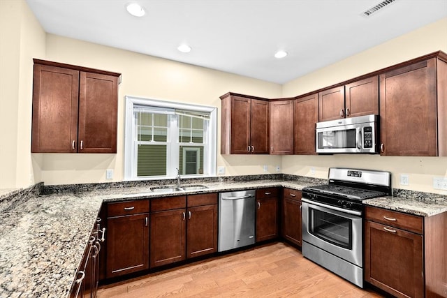 kitchen featuring light wood finished floors, stone countertops, visible vents, appliances with stainless steel finishes, and a sink