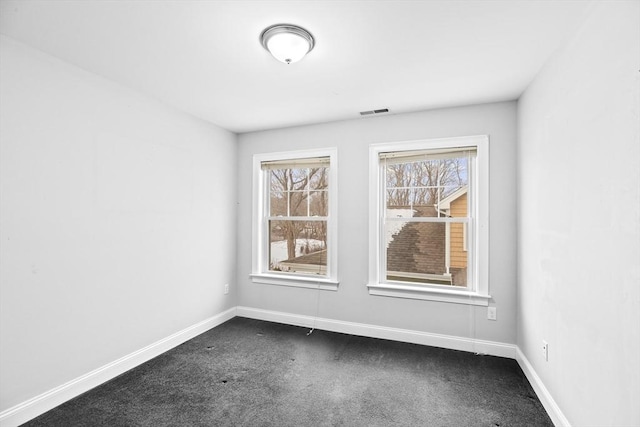 spare room featuring dark colored carpet, visible vents, plenty of natural light, and baseboards