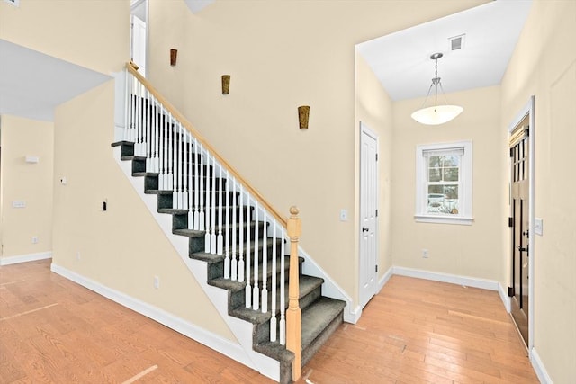 foyer with visible vents, baseboards, light wood-style flooring, stairway, and a high ceiling