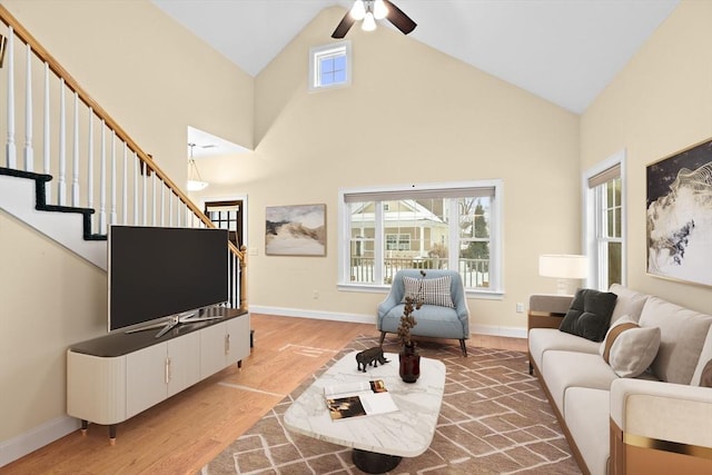 living room featuring stairs, high vaulted ceiling, light wood-type flooring, and baseboards