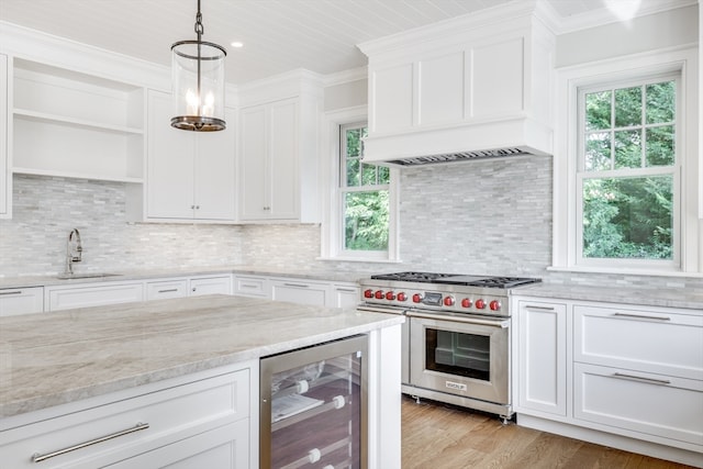 kitchen featuring beverage cooler, white cabinets, sink, premium range, and decorative light fixtures