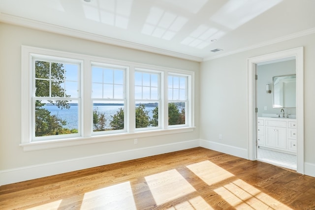 spare room featuring ornamental molding, a water view, sink, and light hardwood / wood-style floors