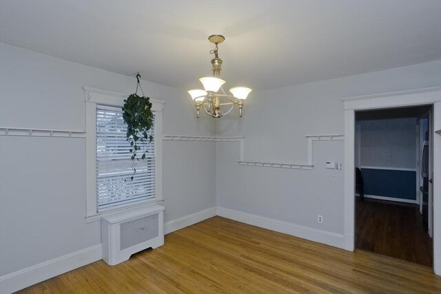 unfurnished dining area featuring a chandelier, radiator heating unit, wood finished floors, and baseboards