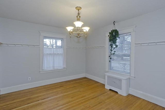 spare room featuring light wood-type flooring, radiator, a notable chandelier, and baseboards