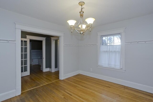 unfurnished dining area with a notable chandelier, baseboards, and hardwood / wood-style flooring