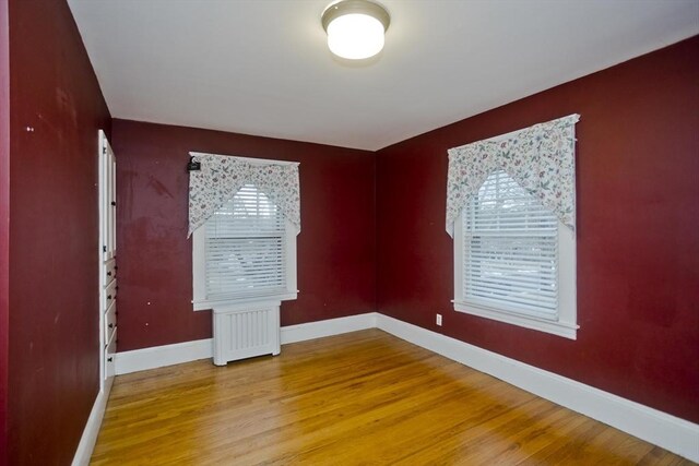 unfurnished bedroom featuring radiator heating unit, multiple windows, wood finished floors, and baseboards