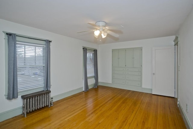 unfurnished bedroom featuring radiator, light wood finished floors, baseboards, and a ceiling fan