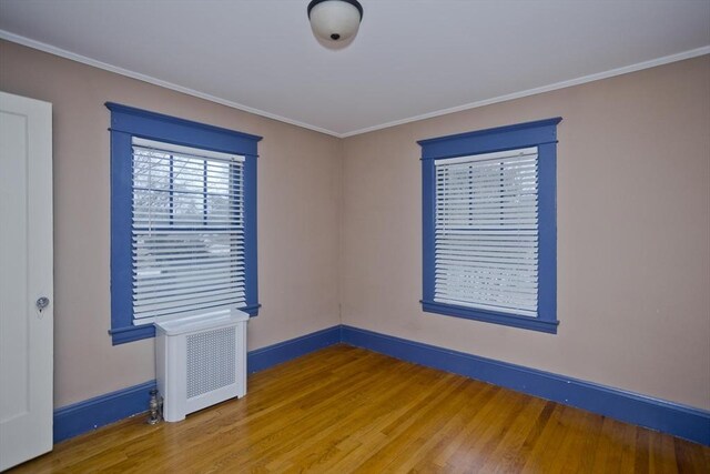 unfurnished room with crown molding, baseboards, wood finished floors, and radiator