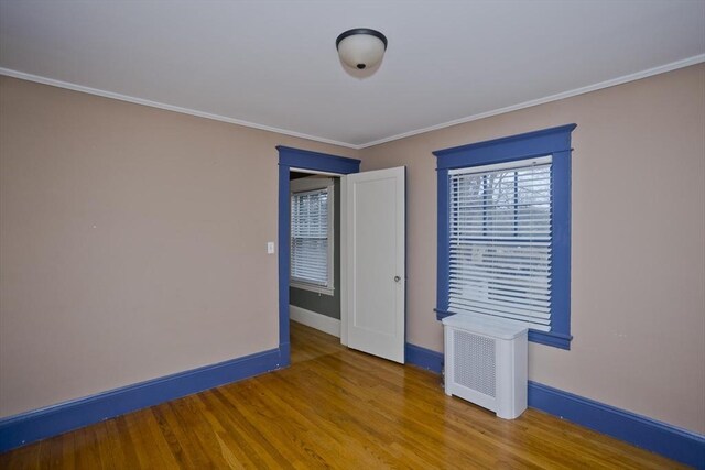 unfurnished room with ornamental molding, radiator, baseboards, and wood finished floors