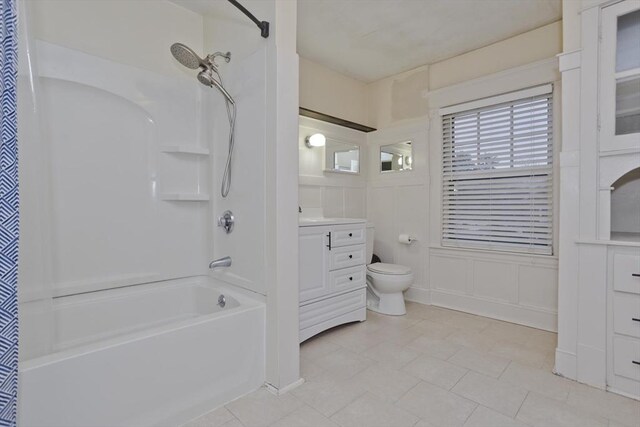 bathroom featuring toilet, shower / bathtub combination with curtain, a decorative wall, and vanity