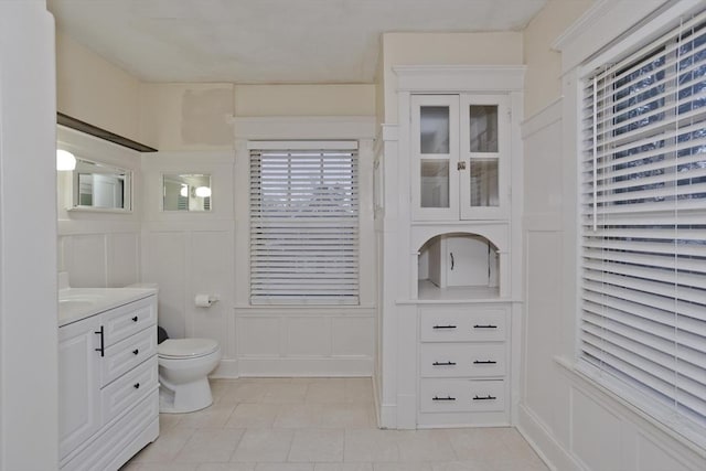 bathroom featuring a decorative wall, vanity, toilet, and tile patterned floors