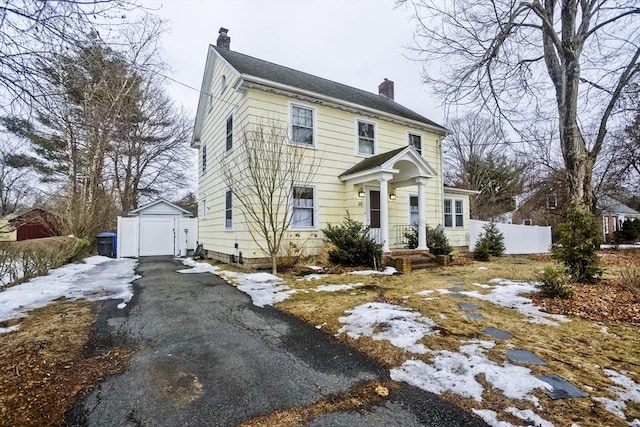 view of front facade featuring aphalt driveway, a chimney, fence, a garage, and an outdoor structure