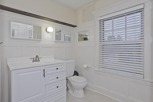 bathroom featuring toilet, tile patterned floors, a decorative wall, and vanity