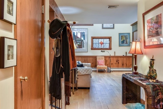 interior space with baseboard heating, light hardwood / wood-style floors, and wood walls