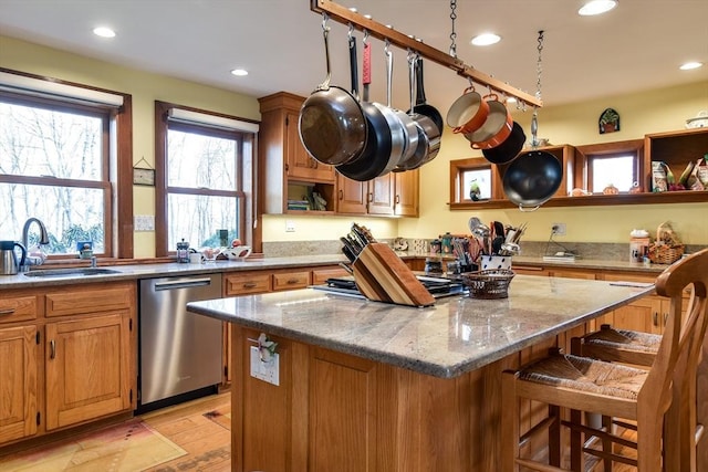 kitchen with a kitchen bar, sink, light stone counters, a center island, and dishwasher