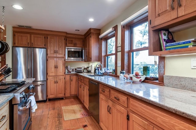 kitchen featuring high end appliances, light stone countertops, sink, and light wood-type flooring