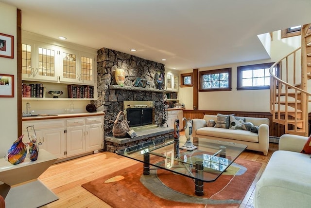 living room featuring indoor wet bar, a stone fireplace, light hardwood / wood-style flooring, and a baseboard heating unit