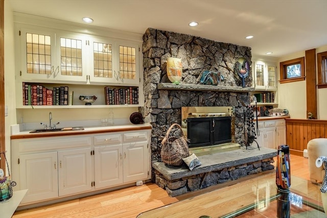 bar with white cabinetry, sink, a fireplace, and light hardwood / wood-style floors