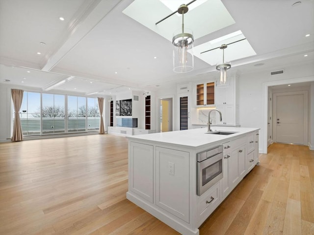 kitchen featuring light wood finished floors, a skylight, a sink, and visible vents