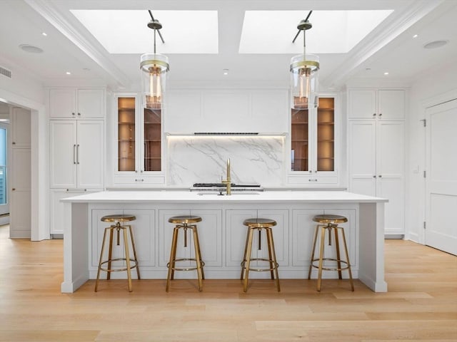 kitchen with light countertops, a sink, a large island with sink, and white cabinets