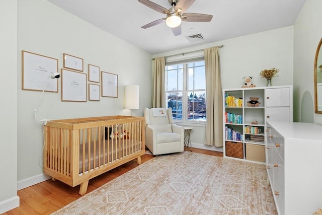 bedroom featuring ceiling fan, a nursery area, and light wood-type flooring