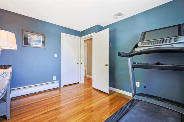 exercise area featuring a baseboard heating unit, wood finished floors, and baseboards