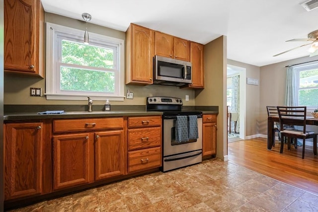 kitchen with appliances with stainless steel finishes, a sink, dark countertops, brown cabinets, and a ceiling fan