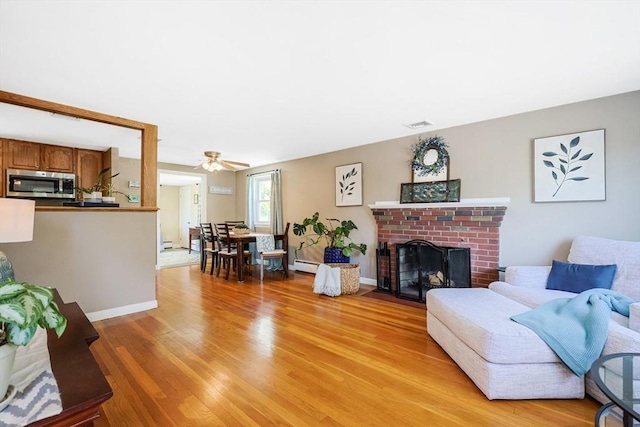 living room with light wood-style flooring, a baseboard radiator, ceiling fan, a fireplace, and baseboards