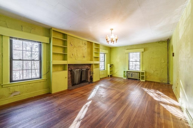 unfurnished living room with dark wood-type flooring, an inviting chandelier, radiator heating unit, a fireplace, and built in shelves