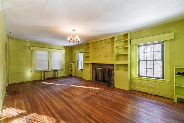 unfurnished living room featuring built in shelves, a chandelier, radiator heating unit, dark hardwood / wood-style floors, and a fireplace