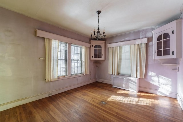 unfurnished dining area featuring hardwood / wood-style flooring, radiator heating unit, and an inviting chandelier