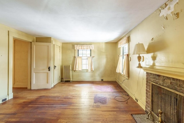 unfurnished living room with wood-type flooring, radiator, and a brick fireplace