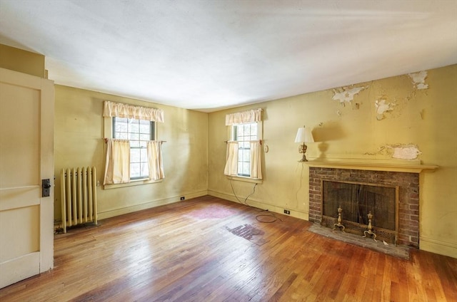 unfurnished living room with a healthy amount of sunlight, a fireplace, radiator, and hardwood / wood-style floors