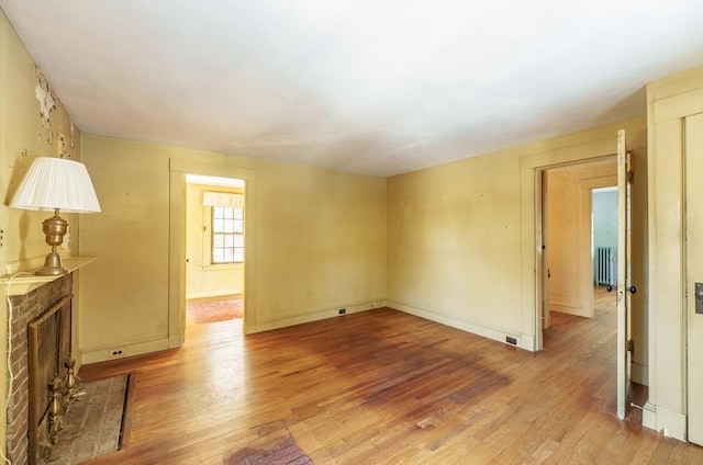 spare room featuring radiator heating unit, a fireplace, and light wood-type flooring