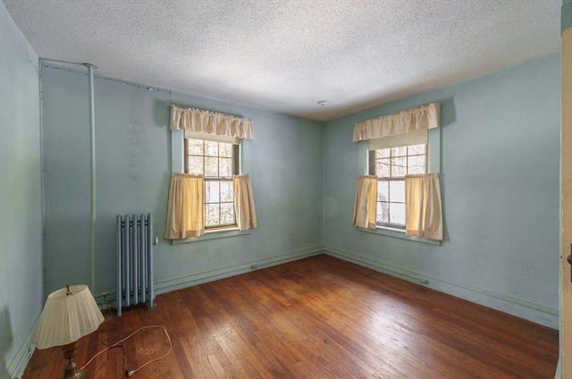 unfurnished room with dark wood-type flooring, radiator heating unit, a textured ceiling, and plenty of natural light