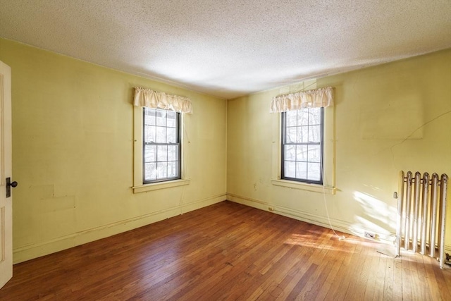 empty room featuring wood-type flooring, plenty of natural light, radiator, and a textured ceiling