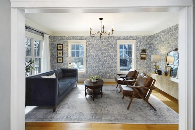 living area with wallpapered walls, crown molding, an inviting chandelier, and wood finished floors