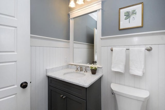 half bathroom with wainscoting, vanity, and toilet