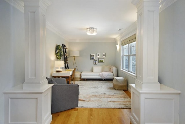 living area featuring light wood finished floors, ornate columns, and ornamental molding