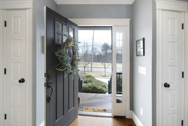 foyer entrance featuring crown molding, wood finished floors, and baseboards