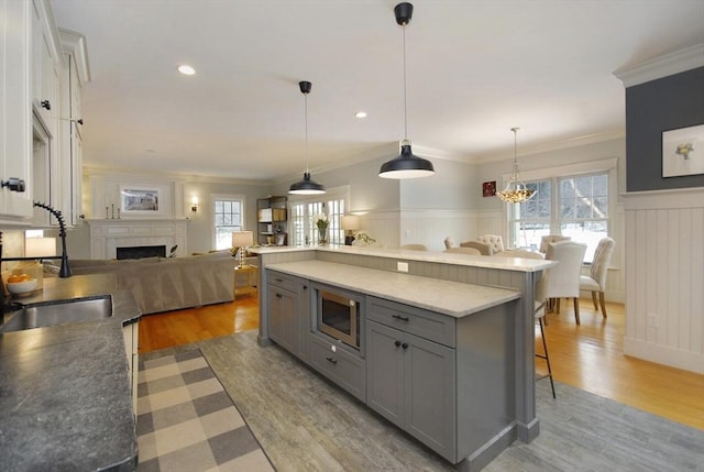 kitchen featuring gray cabinets, a sink, stainless steel microwave, a kitchen breakfast bar, and a fireplace